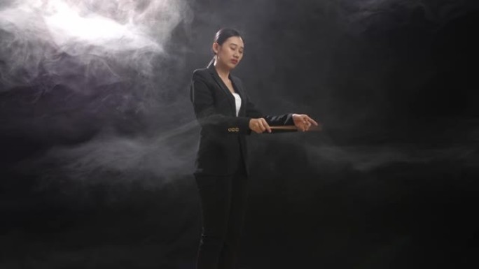 亚洲指挥家女子手持指挥棒，在迷雾笼罩的黑色工作室中迅速展示手势的侧视图