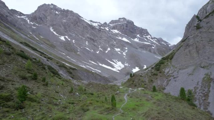 空中无人机镜头直线上升，揭示了冰川山脉景观，积雪成片，孤立的树木是瑞士偏远的高山远足径。