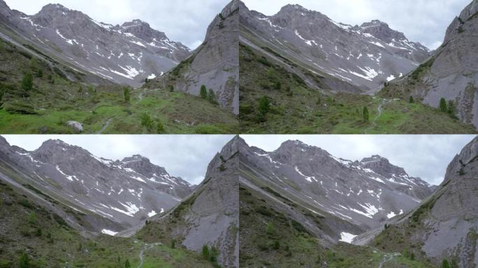 空中无人机镜头直线上升，揭示了冰川山脉景观，积雪成片，孤立的树木是瑞士偏远的高山远足径。
