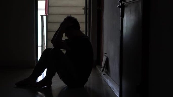 一个紧张的男人的剪影坐在黑暗中，靠在旧公寓的台阶上，失去了生命，暴力，抑郁和自杀的概念。