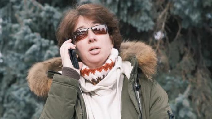 开朗的成熟女人在冬季城市公园通过电话交谈