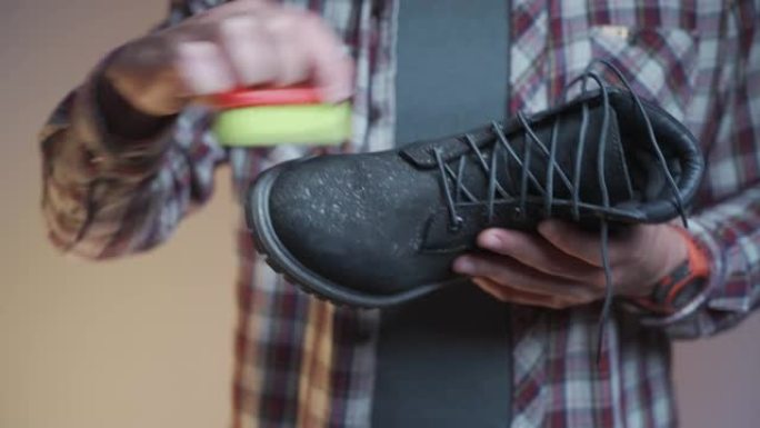 男人在工作室用刷子清洁黑色靴子。男性用小擦洗刷刷磨砂鞋。冬季鞋子护理主题。洗肮脏的黑色秋季短靴，车间