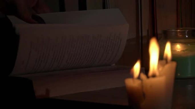 妇女的手在烛光下翻阅一本旧书