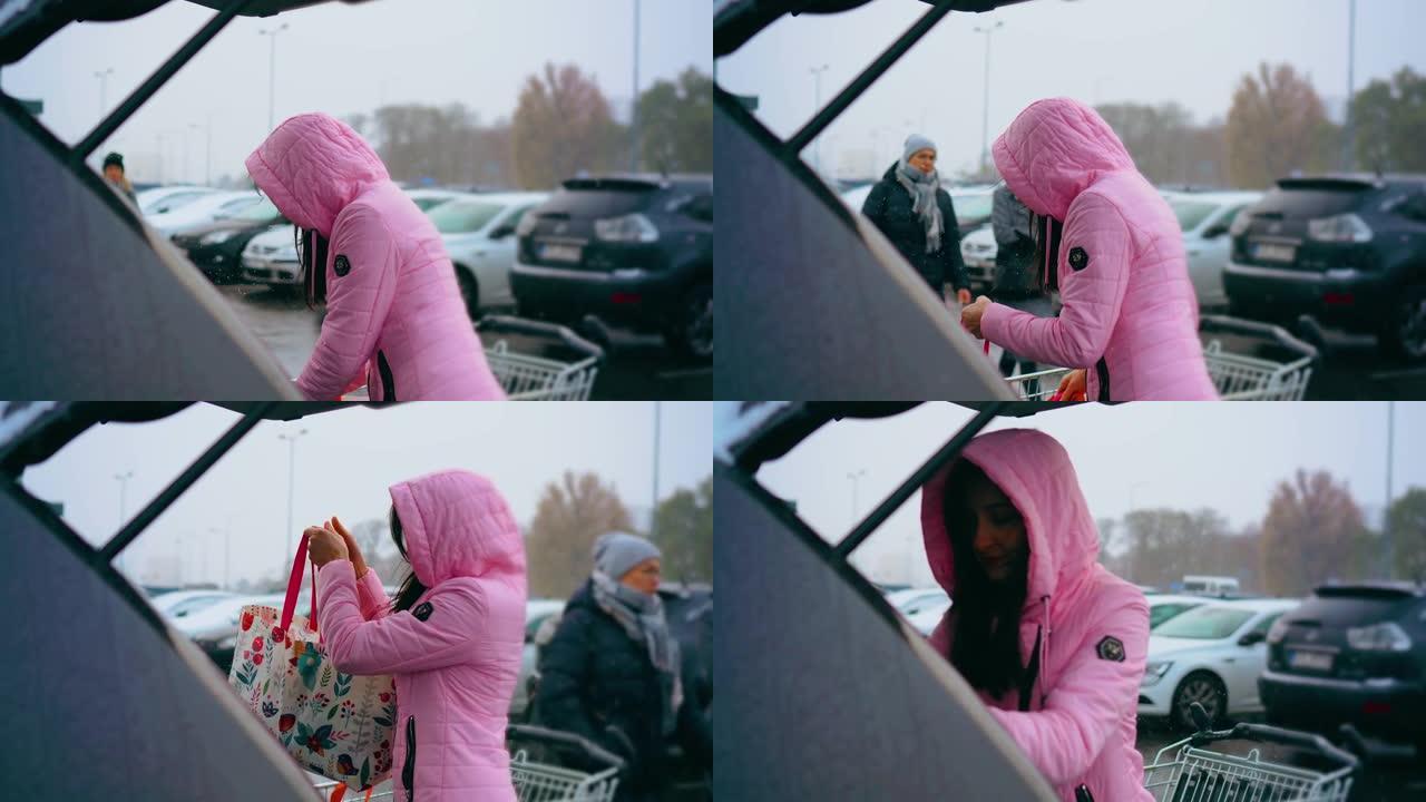 女人在冬天降雪的情况下，将生态袋从市场手推车放到汽车后备箱中。商店购物、销售、折扣