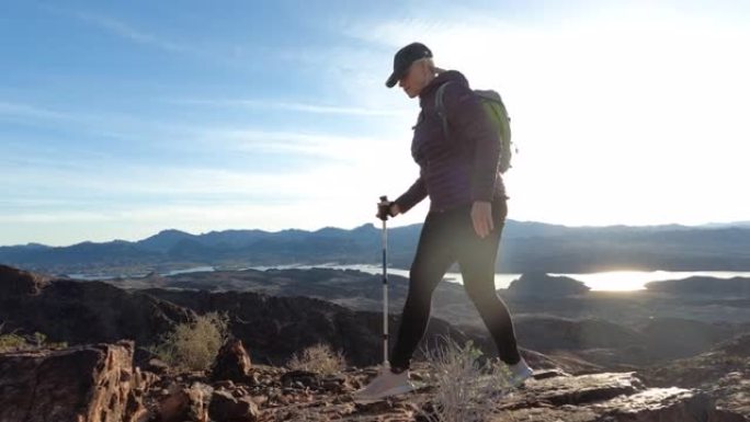 成熟的女人沿着沙漠山脊峰徒步旅行，使用杆子