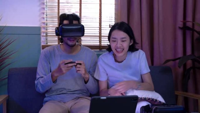 亚洲男子在客厅的房子里戴着虚拟现实护目镜。戴着耳机观看的人感到高兴。带笔记本电脑屏幕照明的家庭内部。