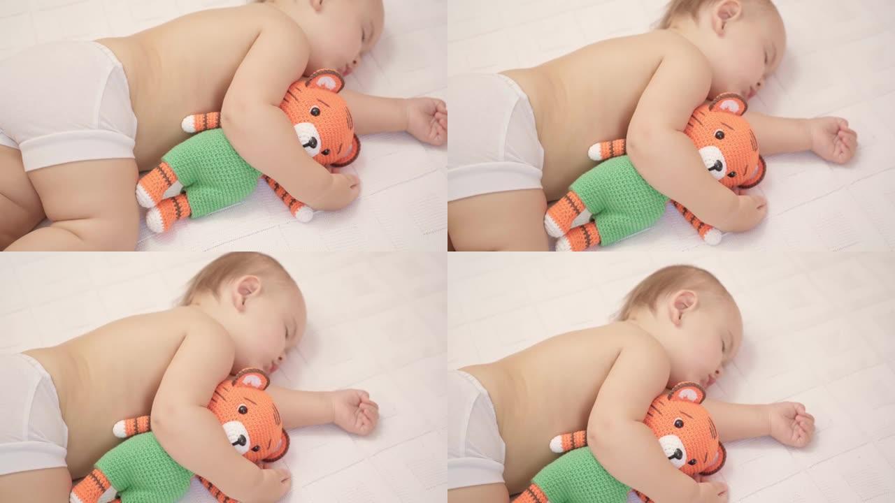 12-17个月大的幼儿睡在床上，抱着一个针织老虎玩具。顶视图