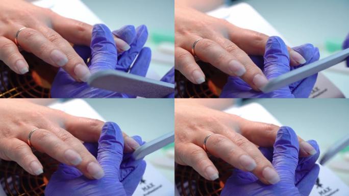 美甲大师的特写蓝色手套用特殊指甲锉锉指甲。