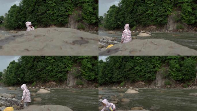 山河上的学龄前儿童。穿着雨衣的男孩女孩向河边扔石头。伙计们从岸上把鹅卵石扔进水里。度假，前往营地，春