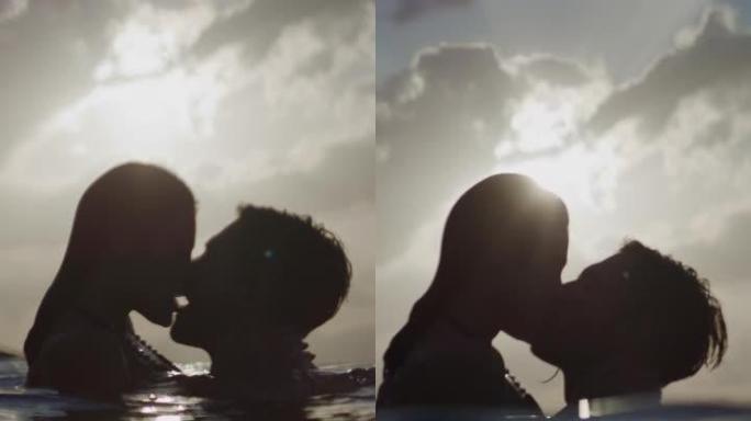 浪漫的异性恋夫妇在美丽的金色日落时在海里游泳。接吻和拥抱一起垂直视频