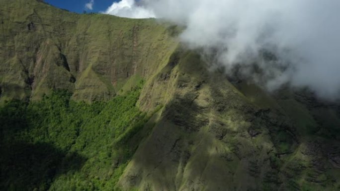 从上方可以看到，令人惊叹的鸟瞰图是绿色的山脉，周围环绕着云层，背景是美丽的蓝天。印度尼西亚西努沙登加