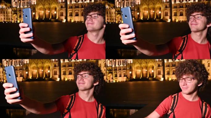 布达佩斯，匈牙利，2022年8月。议会的夜间录像。一个年轻人用手机自拍的肖像。