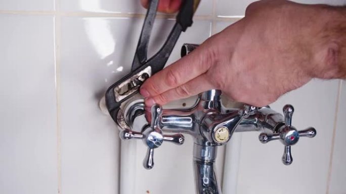 水管在水龙头安装时用可调扳手拧紧螺母。男性双手特写。