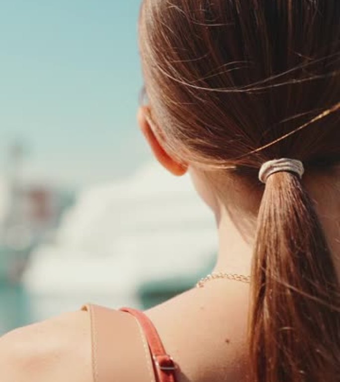 垂直视频: 特写可爱的女人在海港背景上行走。女孩喜欢看游艇和轮船的好天气和美丽的景色。后视图