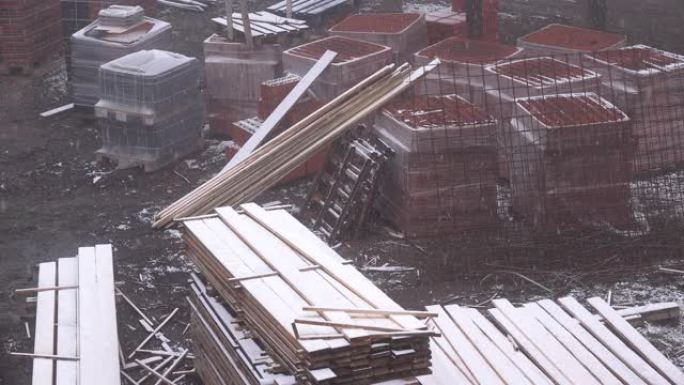 降雪期间建筑工地上的建筑材料 -- 木板、砌块和屋面瓦