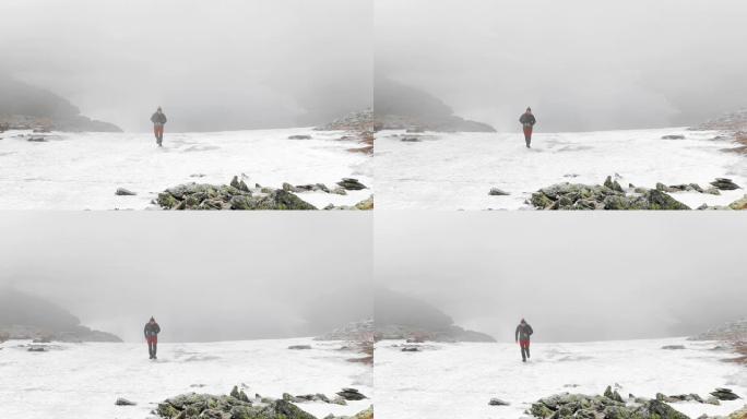 单人男徒步旅行者在罗马尼亚白雪皑皑的法加拉斯山上行走，背景为阴沉的雾