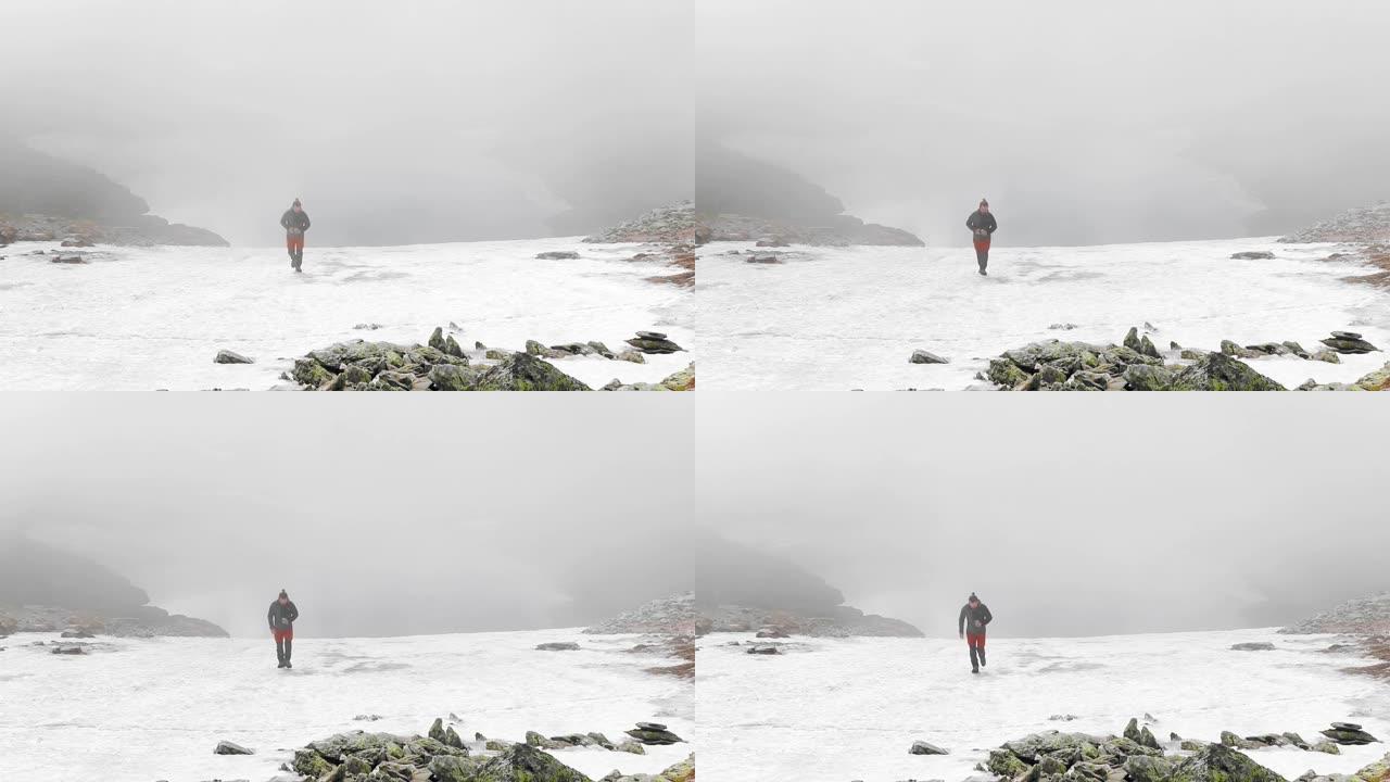 单人男徒步旅行者在罗马尼亚白雪皑皑的法加拉斯山上行走，背景为阴沉的雾