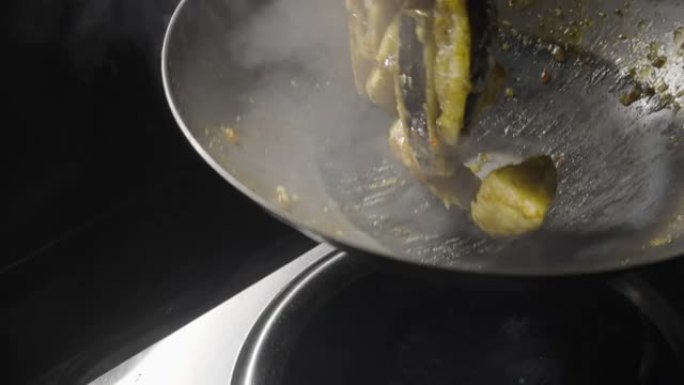 一家亚洲餐厅的厨师在热煎锅里炸茄子，把它们扔到厨房的背景下。男人用热香料，大蒜和糖浆在油中炸蔬菜。慢