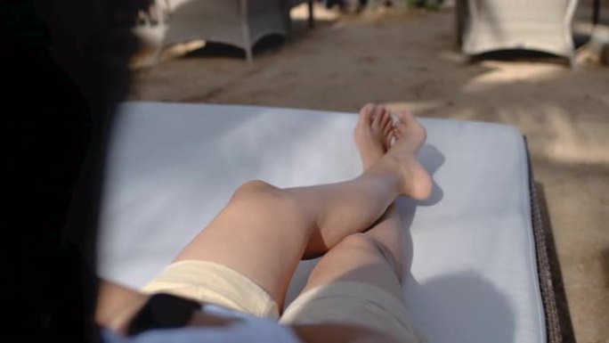 关闭躺在海上沙滩床椅子上的赤脚交叉腿