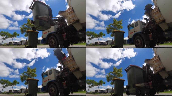 垃圾车机械臂抬起红色轮式垃圾箱并倾倒垃圾的低角度视图。