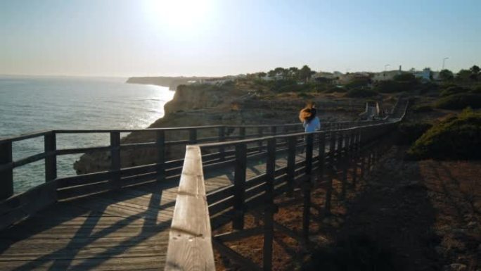 葡萄牙阿尔加维的一个旅游女孩在日落时在木桥上奔跑。