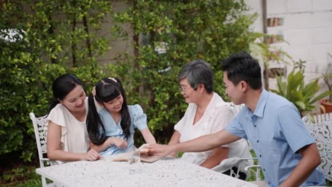 微笑的亚洲多代家庭和十几岁的女孩在一起度过有趣的时光，同时在家里的后院一起聊天和阅读