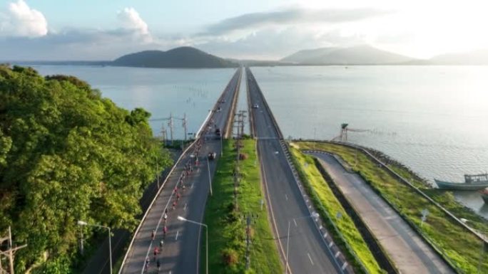 日出场景空中无人机在泰国宋卡省宋卡河的桥上拍摄了大批自行车骑行