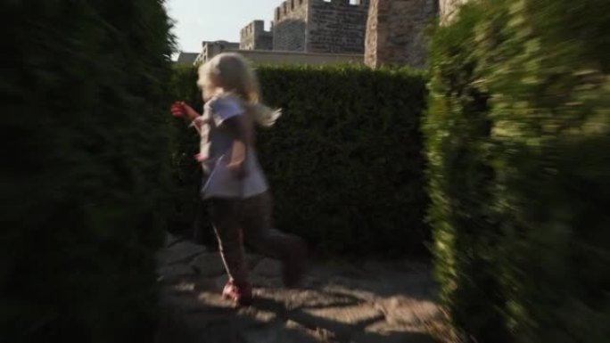 白种人金发小女孩在灌木丛迷宫中逃跑的动作镜头