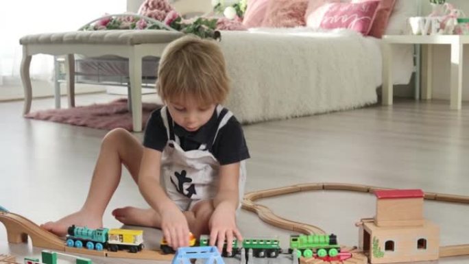 可爱的金发蹒跚学步的孩子，男孩，在家玩五颜六色的火车和铁路