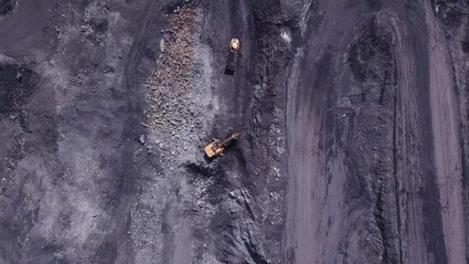 黄矿挖掘机的无人机视图在露天煤矿区将煤炭装载到大型自卸车中。采石场采煤过程的航拍画面。