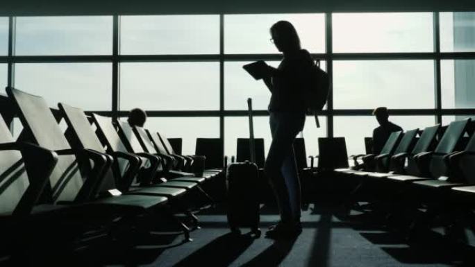 一名女商人站在机场候机楼。使用平板电脑和旅行包