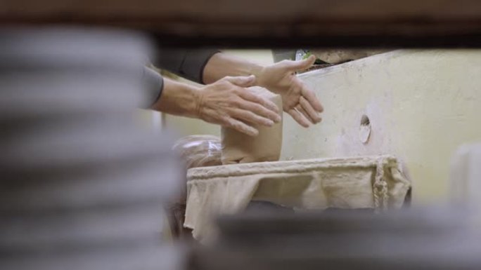 陶工的雄性手揉捏并形成柔软，潮湿的白色粘土片。制作手工罐用粘土材料的制备。制作特写的陶器。慢动作手工