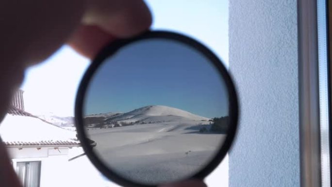 透过圆形有色玻璃可以看到白雪覆盖的山峰。拿着相机的人
ND滤波器并检查其不透明度