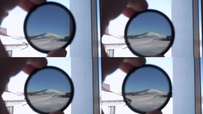 透过圆形有色玻璃可以看到白雪覆盖的山峰。拿着相机的人
ND滤波器并检查其不透明度