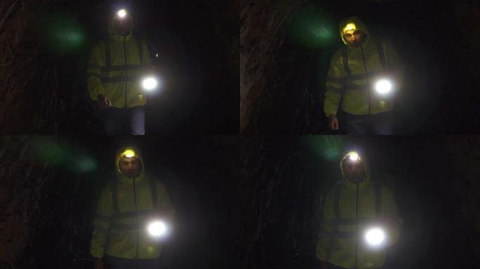 一名男子志愿者的肖像，手里拿着手电筒，额头上拿着手电筒，在一个黑暗的洞穴中寻找失踪人员，缓慢的莫