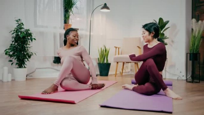 年轻灵活的亚洲和非裔美国女性朋友旋转身体，在家练习瑜伽，打手势namaste