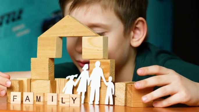 家庭日概念。6-7岁的高加索男孩玩积木，盖房子，梦想一个家庭。家庭铭文。剪纸剪影，儿童游戏。选择性聚