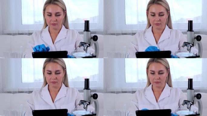 女科学家研究化学家穿着医疗服和防护手套，用平板电脑和显微镜在实验室进行研究