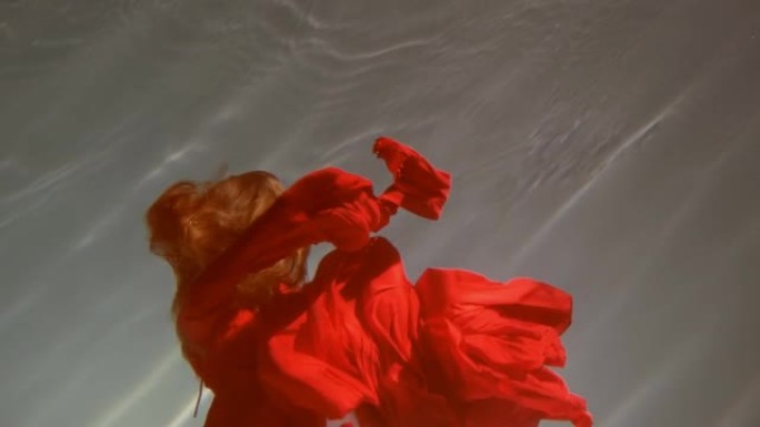 一个美丽的红发年轻女子，她周围漂浮着鲜艳的红色织物，在水下