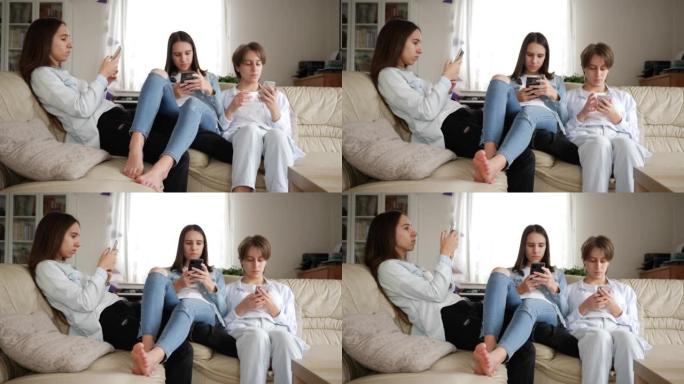 十几岁的女孩三胞胎姐妹在家看着坐在沙发上的社交媒体上的智能手机