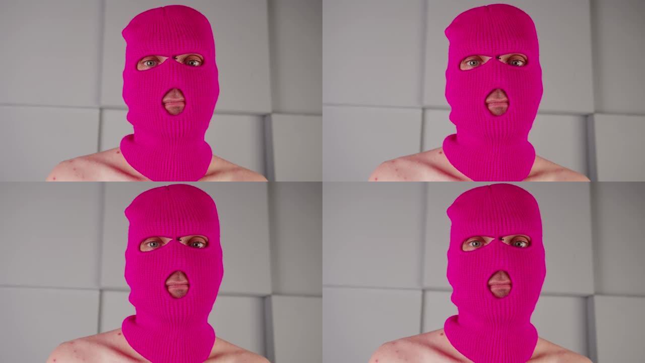 穿着粉色巴拉克拉法帽的面目全非的人的肖像。戴着面具的流氓看着相机
