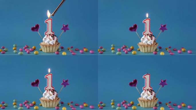 祝1岁宝宝生日快乐，带蜡烛的生日蛋糕和蓝色背景上的生日装饰品。点燃并熄灭纸杯蛋糕上的节日蜡烛