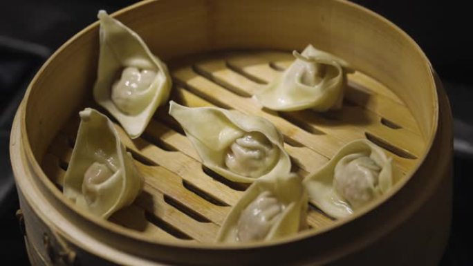一个男人的手打开了展示中国饺子馄饨的竹蒸箱的盖子，在黑色背景上关闭。餐厅中餐。亚洲蒸汽食品点心，馅饺