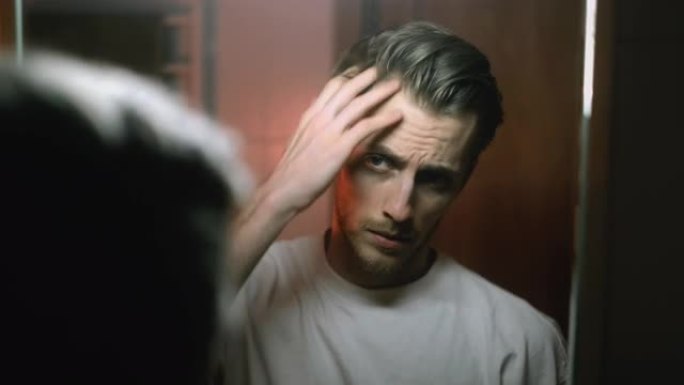 年轻的白人男子站在浴室的镜子上看着自己，做发型。