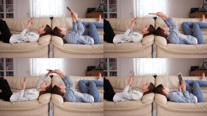 十几岁的女孩双胞胎姐妹在家观看社交媒体上的智能手机躺在沙发上正面交锋
