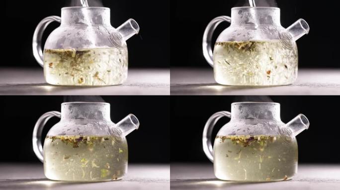 在深色背景下的玻璃透明茶壶中酿造凉茶的过程。将热水倒入带茶叶的水壶中。