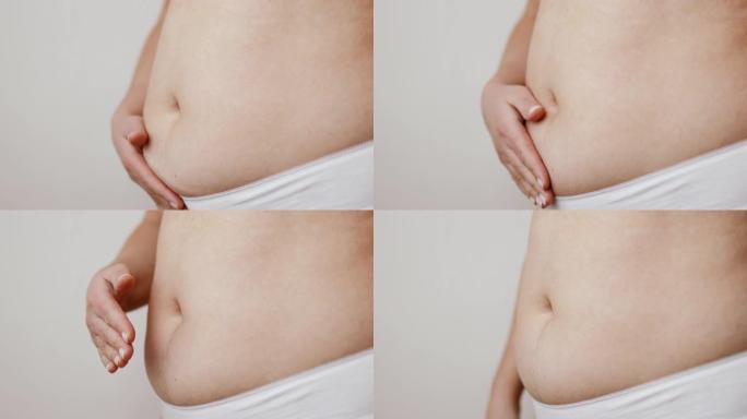特写镜头剪下了无法辨认的胖女人的手，在白色背景上握着肥胖的腹部。