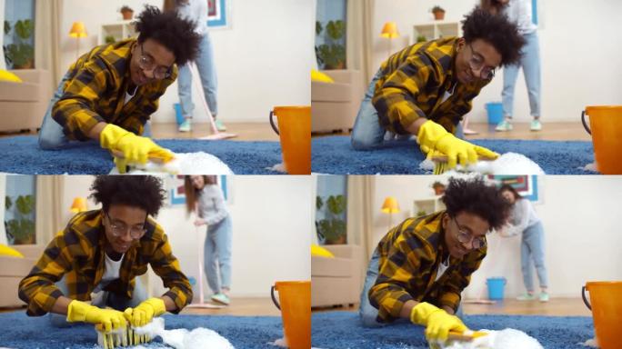 幸福多样的已婚夫妇一起打扫公寓。非裔美国人用洗涤剂和刷子清洁地毯，而女友在背景上拖地