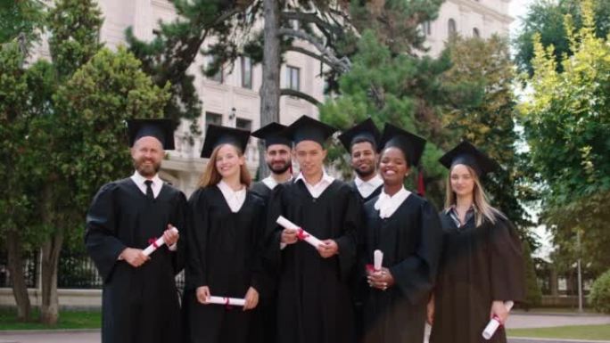 在大学花园毕业日里，一群富有魅力和兴奋的学生在镜头前合影，他们穿着毕业套装和帽子，面带微笑。在阿里·