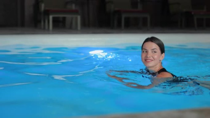 穿着时尚比基尼的迷人女人在酒店游泳池游泳